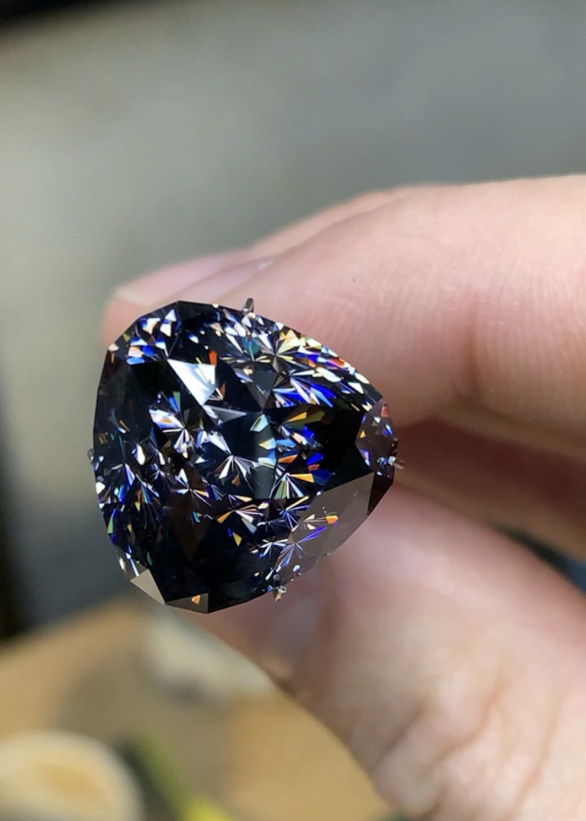 Portrait of a dark grey to black faceted cubic zirconia with blue, yellow, and orange dispersion.